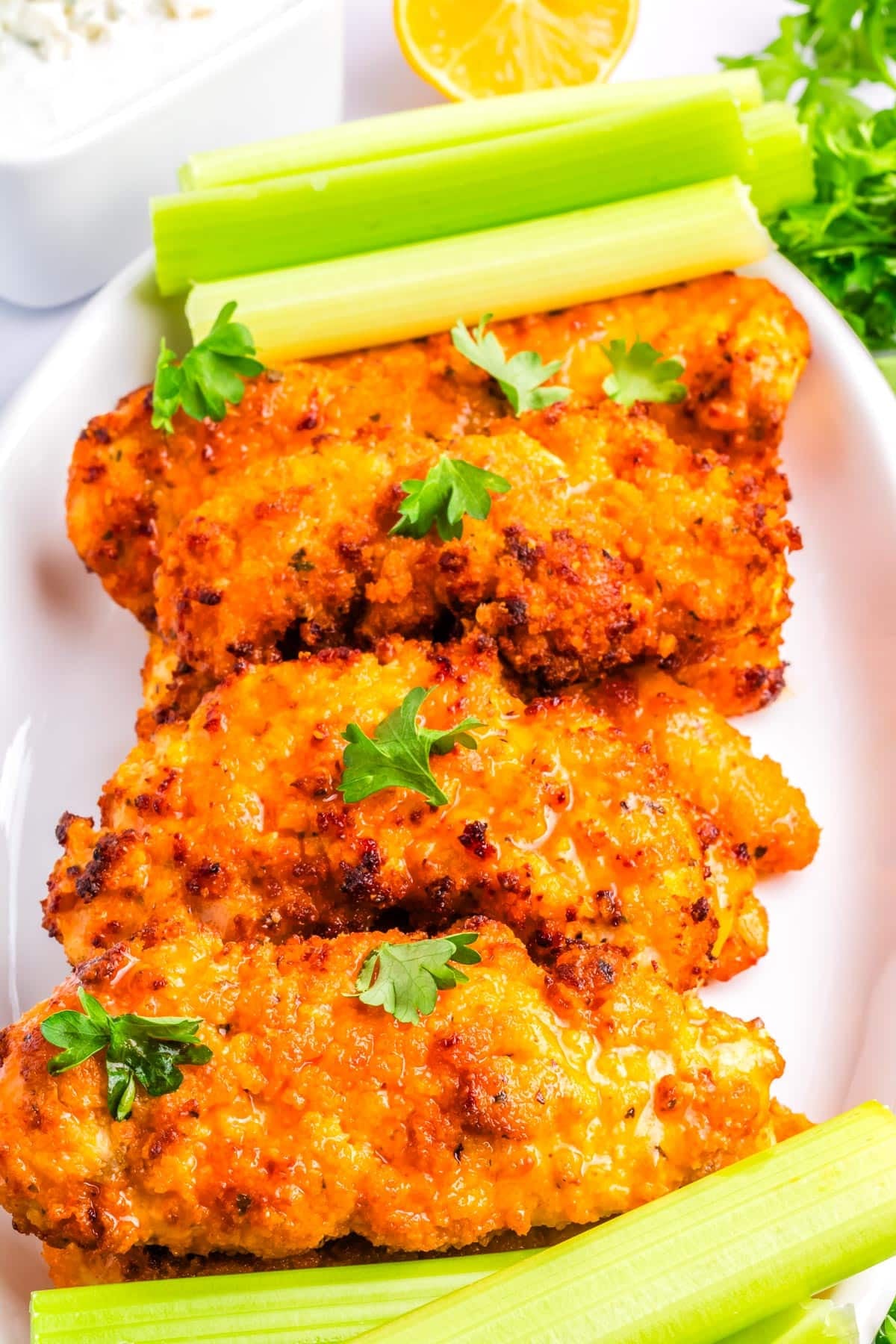 Buffalo chicken tenders stacked on a white serving platter with celery sticks.