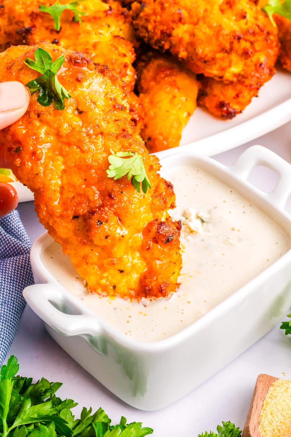A chicken tender dipping into blue cheese dressing.