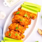 A plate of chicken tenders on a plate with celery sticks and blue cheese dressing in the background.