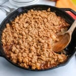 Apple crisp in a skillet with a wooden serving spoon in it.