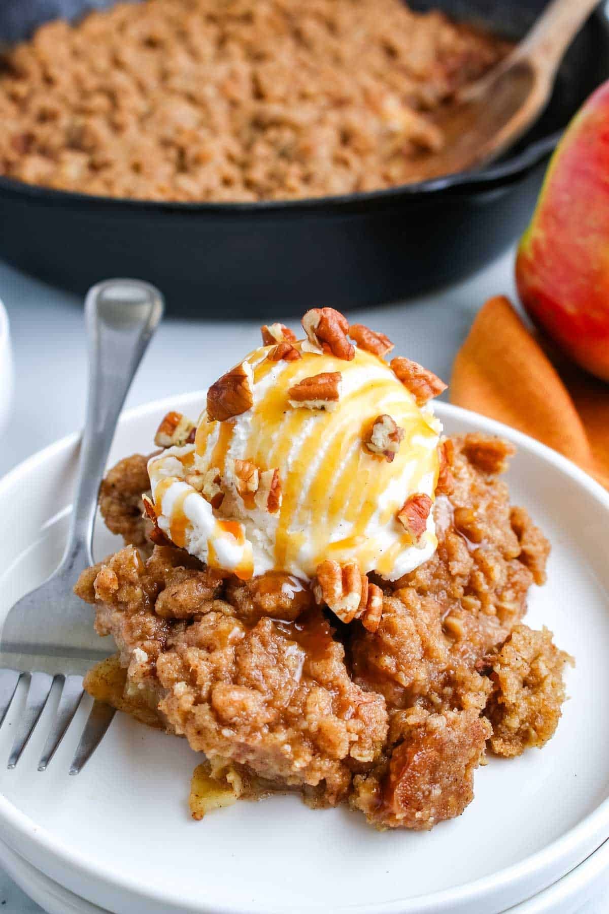 Apple crisp on a white dessert plate topped with ice cream.