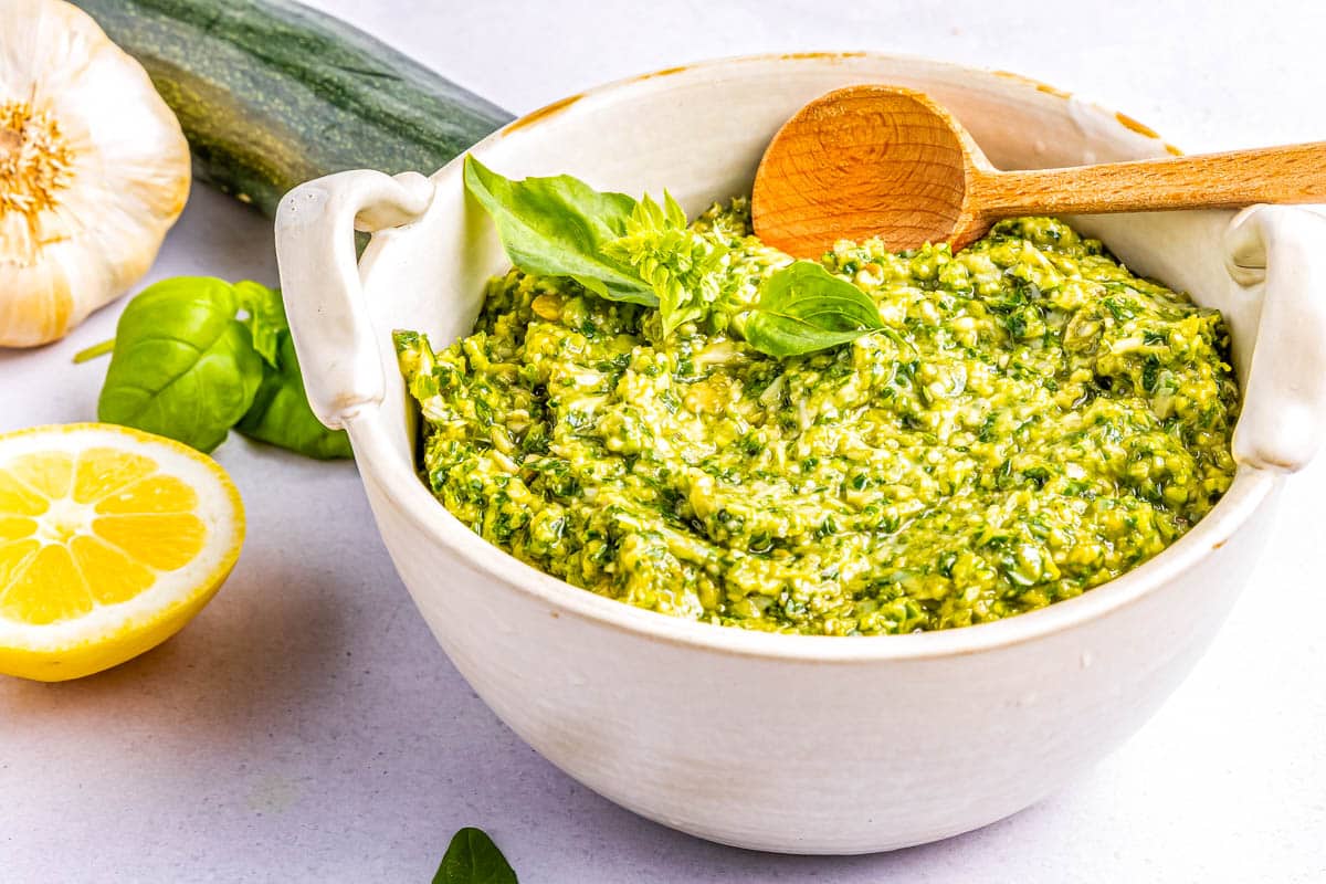 Pesto in a white bowl with a wooden spoon.