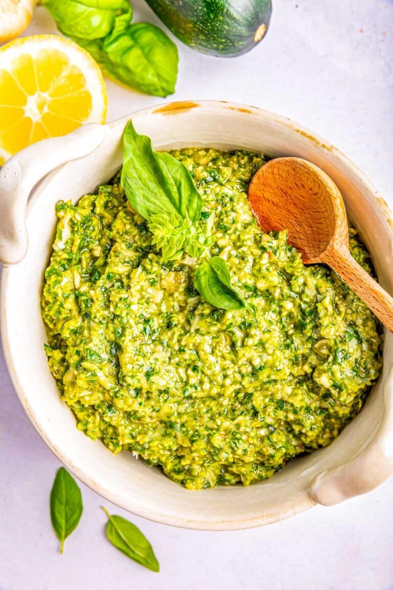 Zucchini Pesto in a white bowl with a wooden serving spoon.