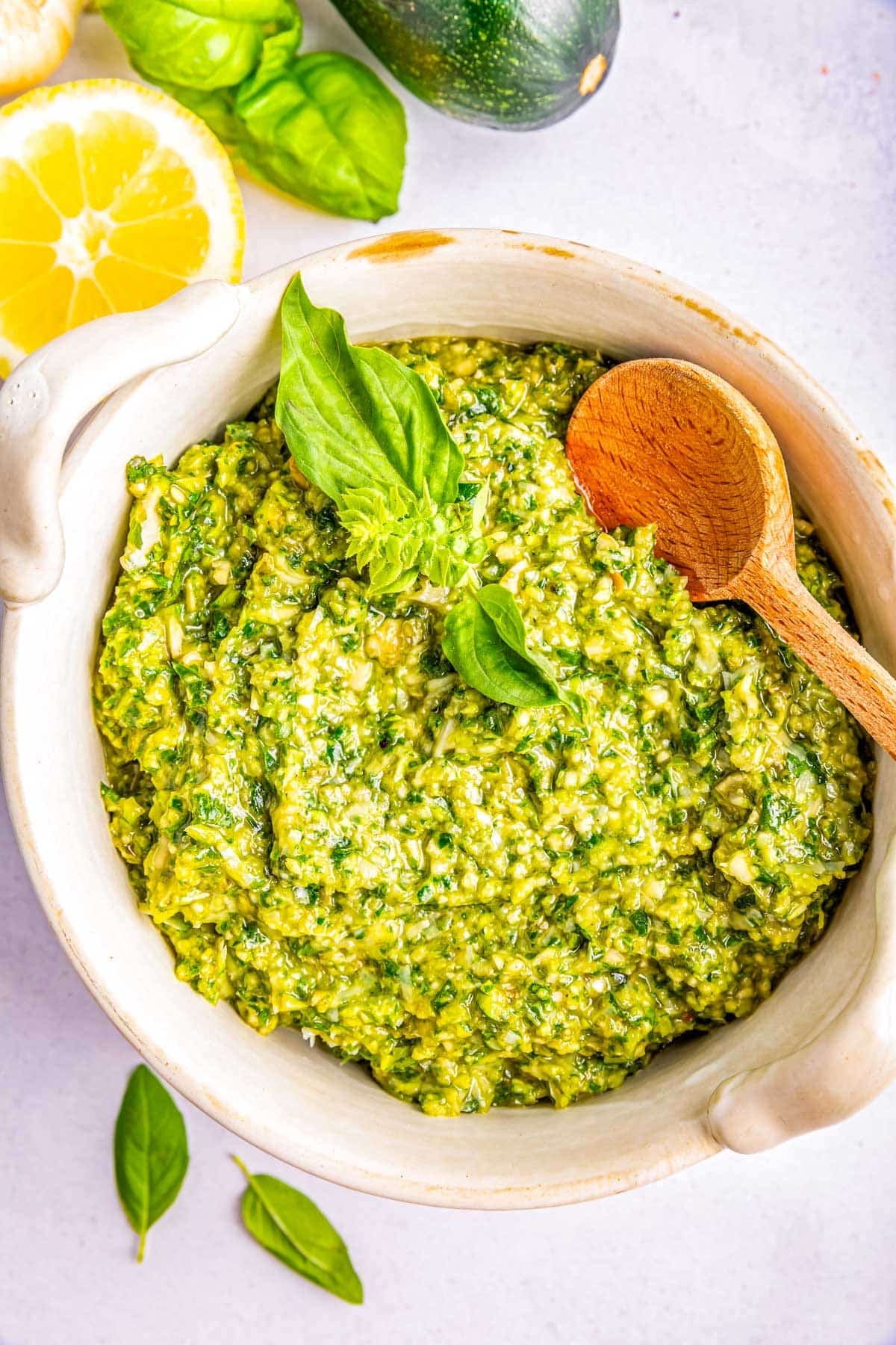 Zucchini Pesto in a white bowl with a wooden serving spoon.