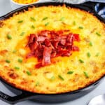 Mashed potatoes in a cast iron skillet and garnished with shredded cheese, crumbled bacon, and chives.