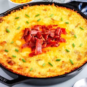 Mashed potatoes in a cast iron skillet and garnished with shredded cheese, crumbled bacon, and chives.