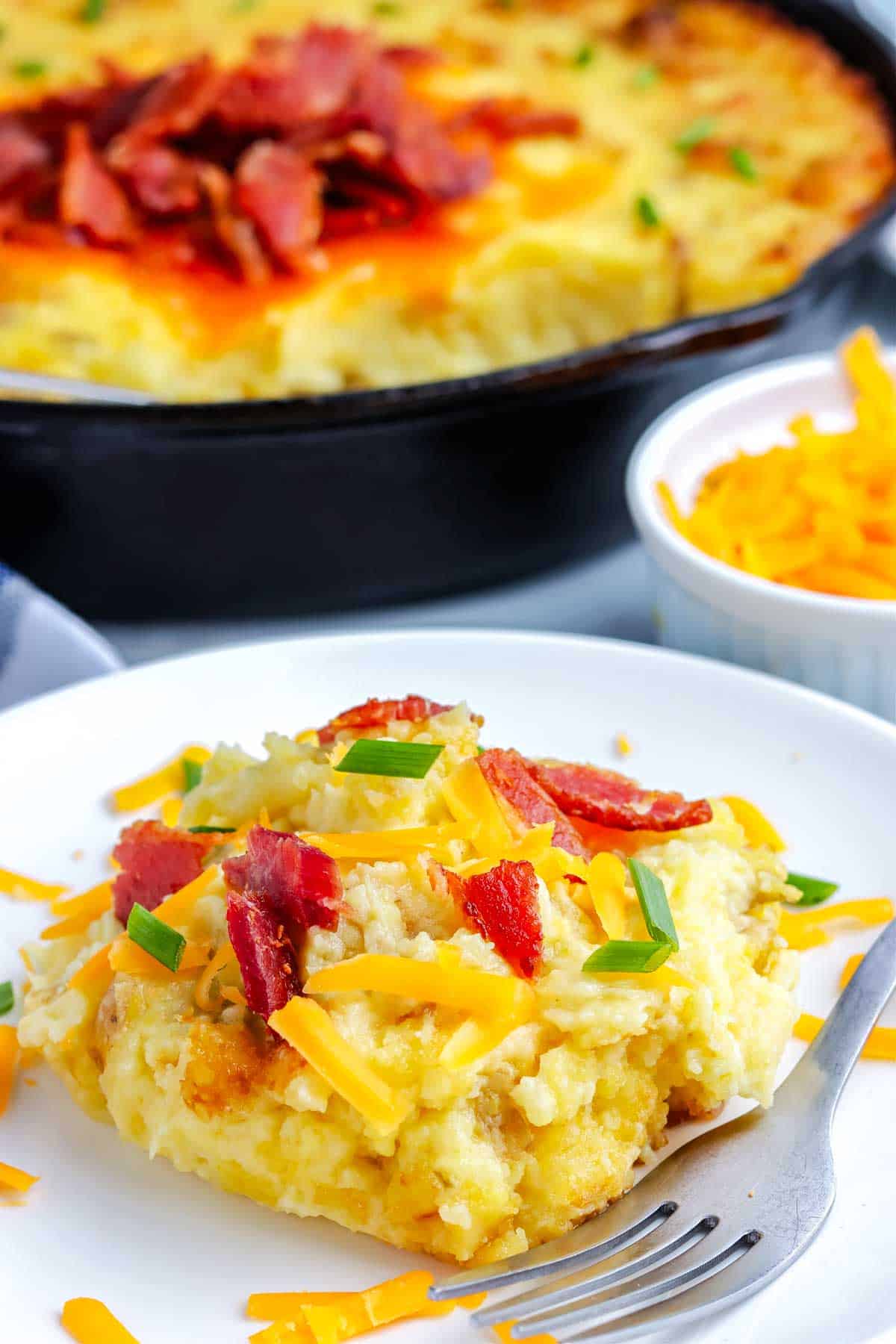 Mashed potatoes on a white plate garnished with cheese, bacon, and chives.