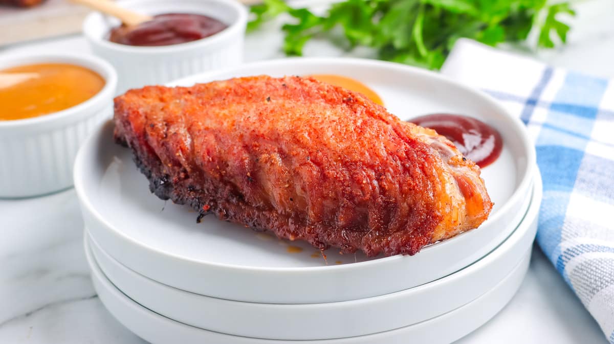 A wing on a small white plate with BBQ sauce on the side.