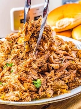 The finished pulled pork being picked up with serving utensils.