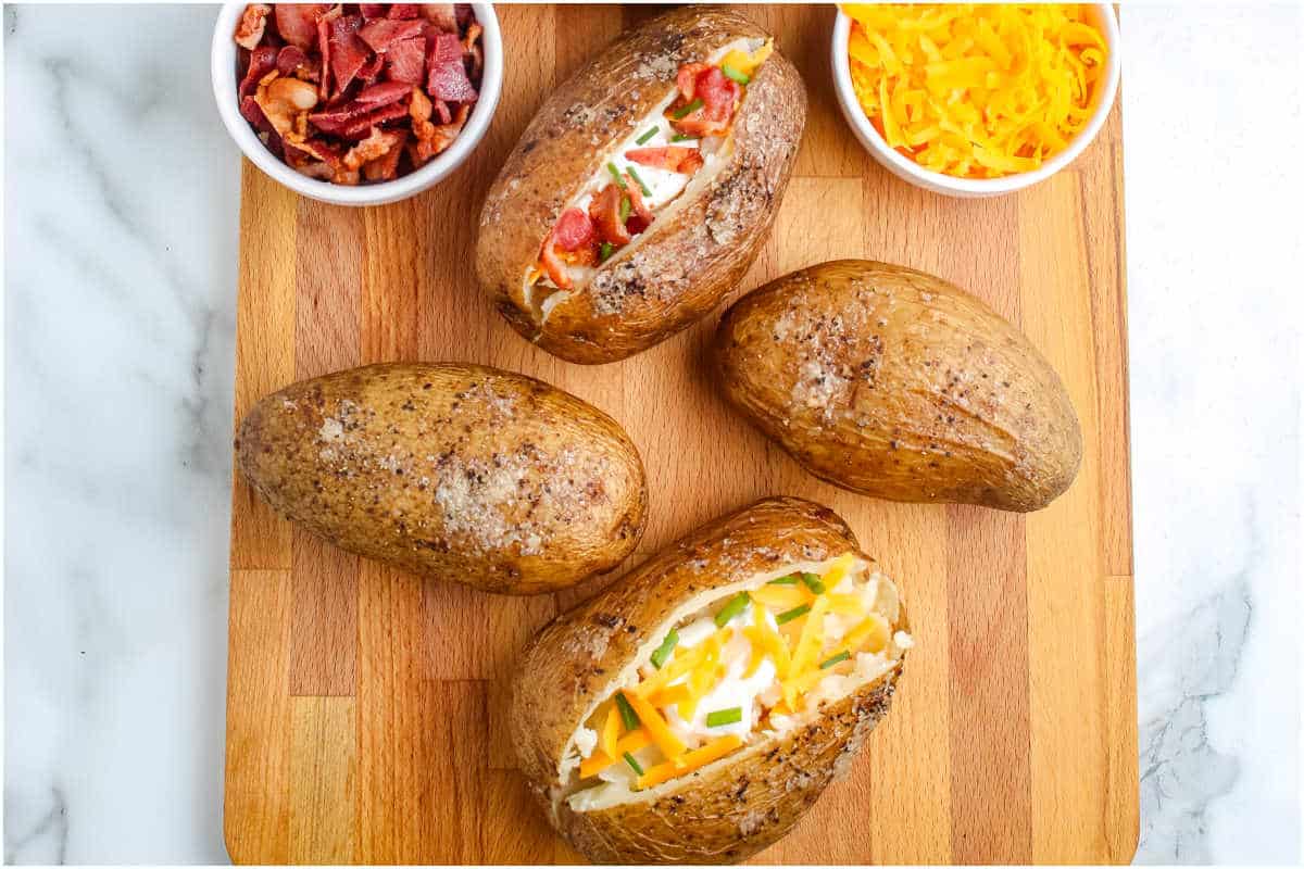 The finished potatoes on a wooden board and dressed with cheese, bacon, and sour cream.