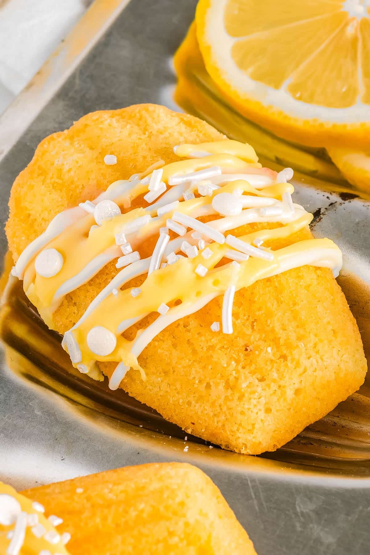A finished Lemon Madeleines drizzled with white chocolate and a lemon curd glaze.