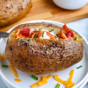 A potato on a white plate with cheese, butter, chives, bacon, and sour cream.