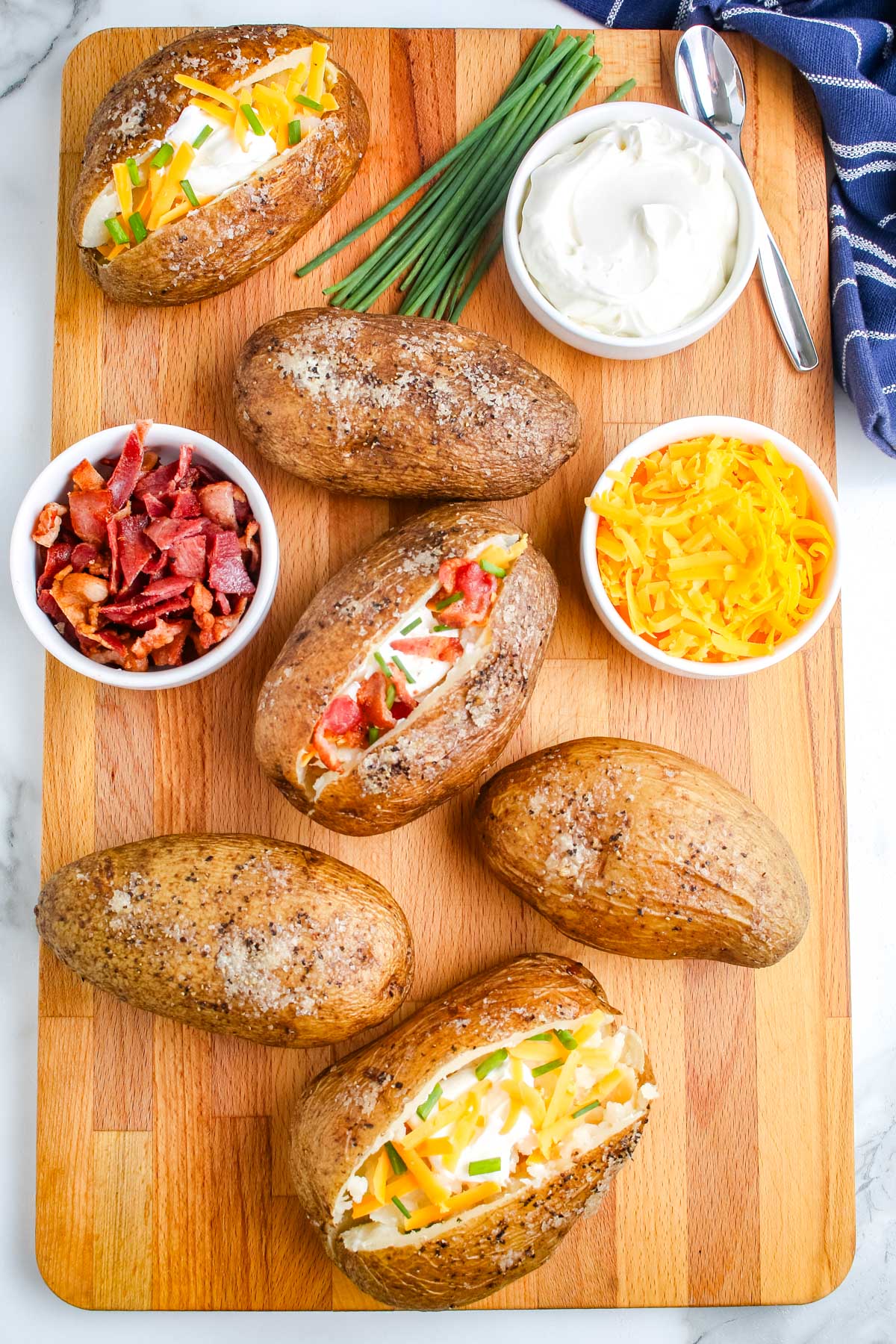 Smoked Baked Potatoes on a wooden board and dressed with cheese, bacon, and sour cream.