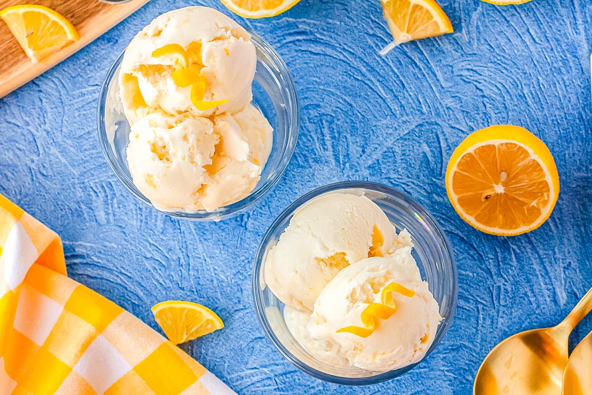 Dishes of the finished lemon sherbet recipe on a tabletop with lemon slices and a decorative napkin nearby.