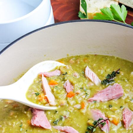 A spoon piking up some of the finished recipe for split pea soup with ham from a Dutch oven.