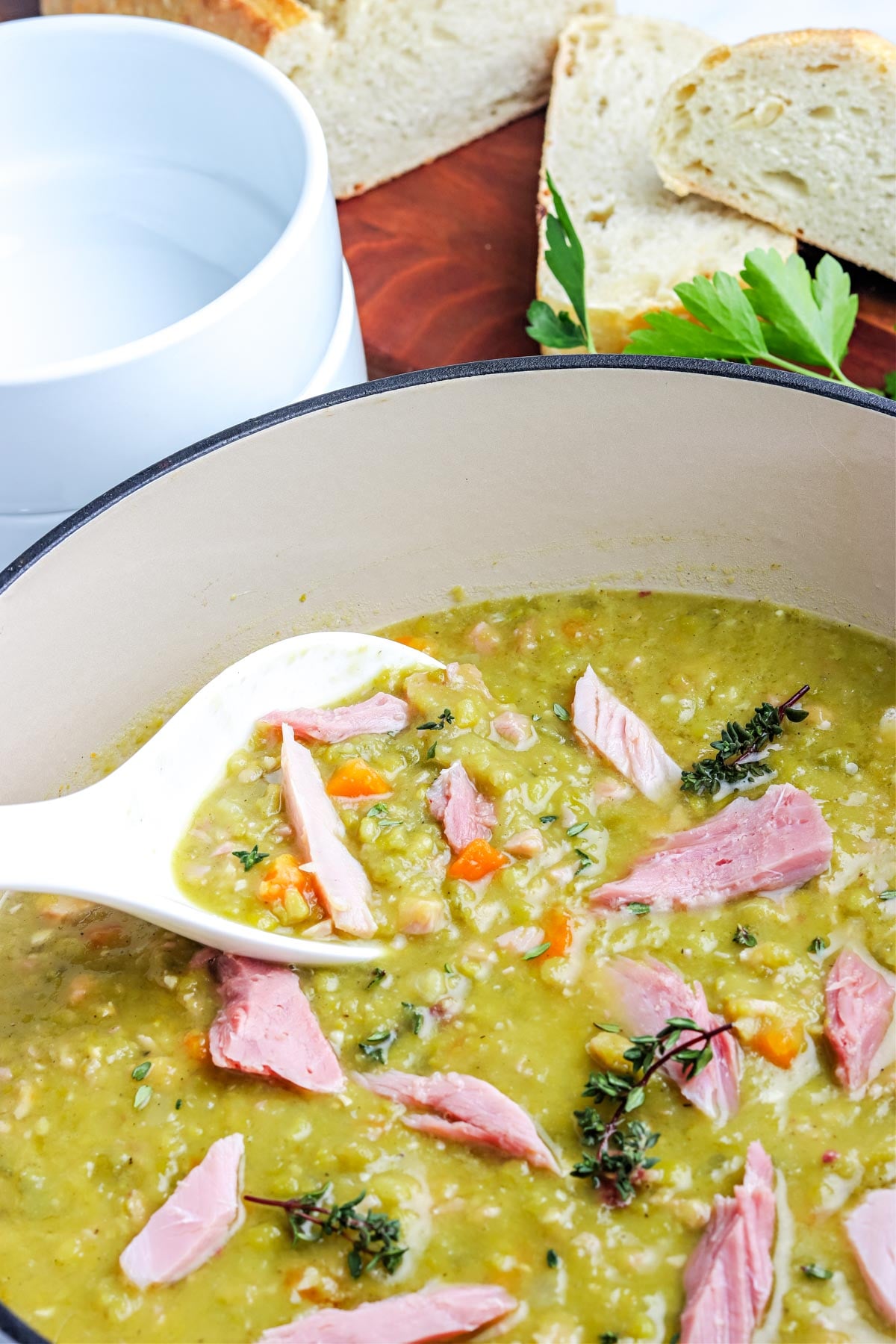 A spoon piking up some of the finished recipe for split pea soup with ham from a Dutch oven.