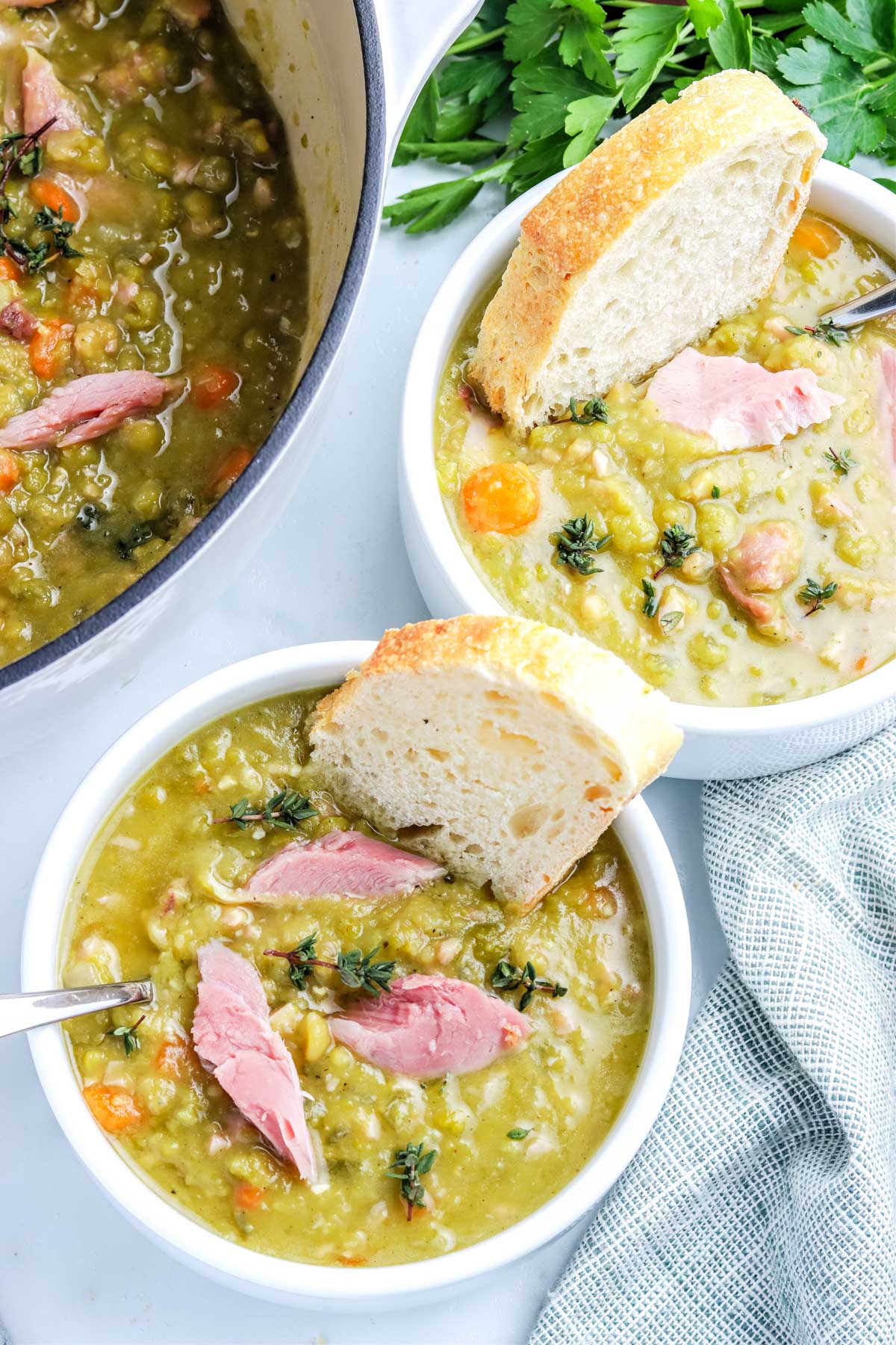 Two bowls of split pea and ham soup with a pot of the soup in the background.