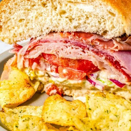 A close up of a grinder sandwich on a plate with potato chips.