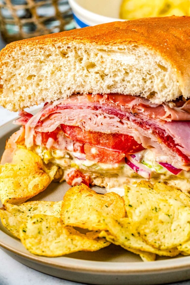 A close up of a grinder sandwich on a plate with potato chips.