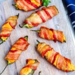 Eight smoked bacon wrapped jalapeno pioppers on a wooden serving board.