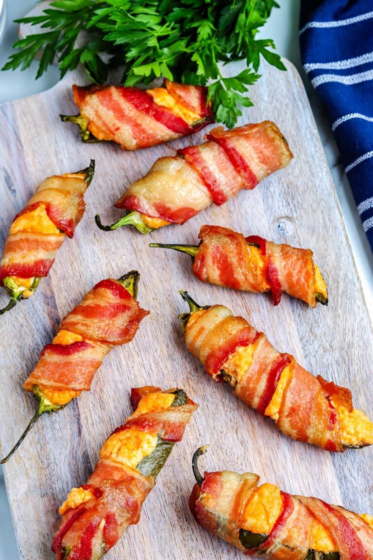 Eight smoked bacon wrapped jalapeno pioppers on a wooden serving board.