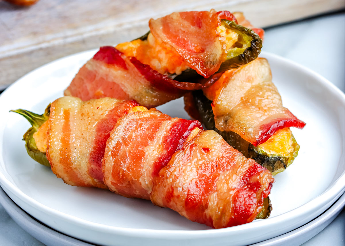 The finished Smoked Jalapeno Poppers wrapped in bacon and on a white serving plate.