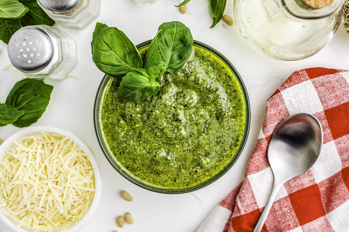 Blender pesto in a glass bowl with a spoon and basil leaves near it.