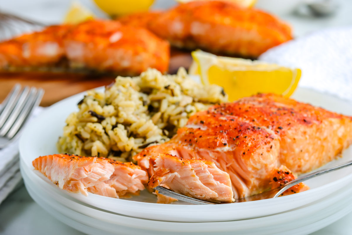 A filet of cedar plank grilled salmon on a white plate with lemon wedges and rice pilaf.