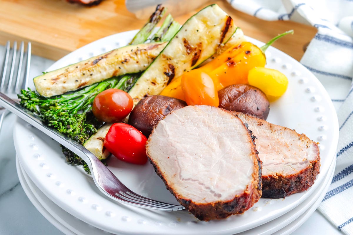 Two slices of grilled boneless pork loin on a plate, along with grilled vegetables.