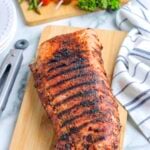 A grilled roast pork loin on a wooden cutting board.