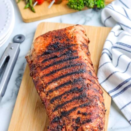 A grilled roast pork loin on a wooden cutting board.
