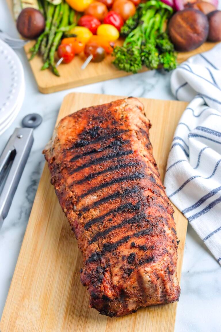 A grilled roast pork loin on a wooden cutting board.