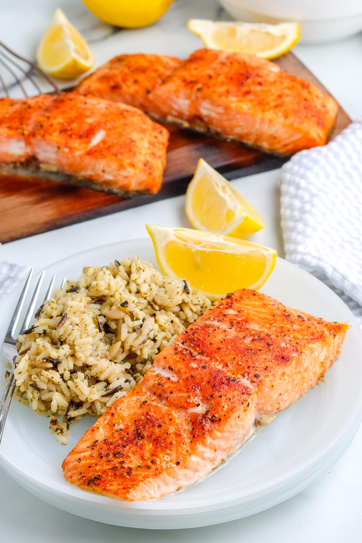 A filet of salmon that was grilled on a cedar plank on a plate with lemon wedges and rice pilaf.