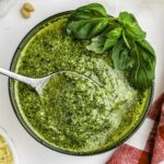 Pesto in a clear glass bowl with a spoon in it.