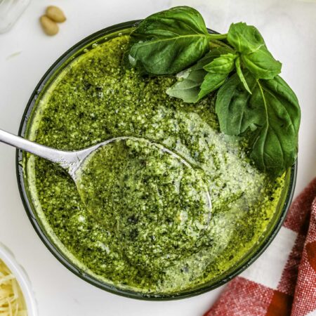 Pesto in a clear glass bowl with a spoon in it.