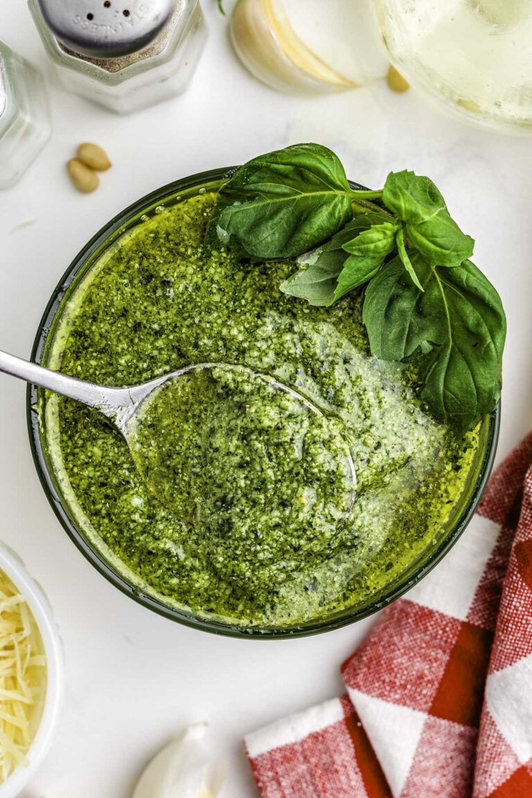 Pesto in a clear glass bowl with a spoon in it.