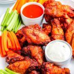 A platter of smoked buffalo wings with blue cheese dressing and buffalo sauce.