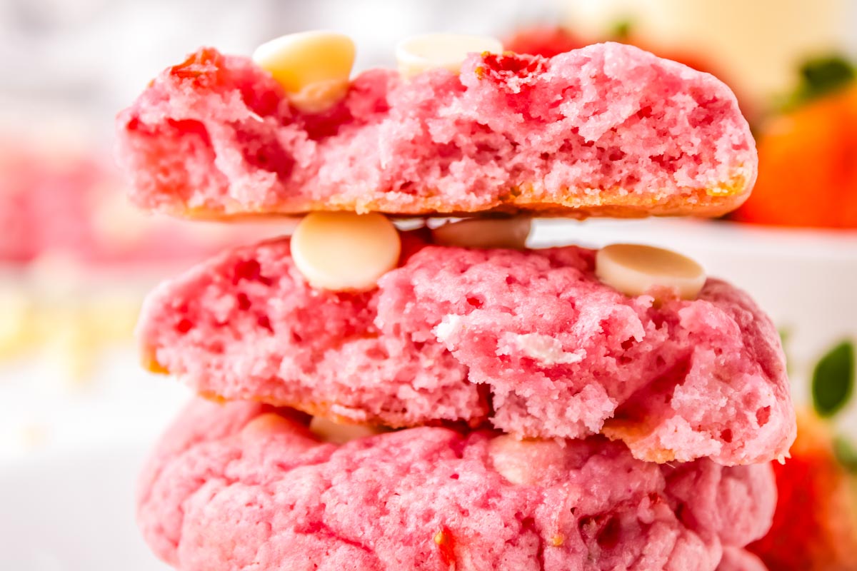 Three strawberry white chocolate cookies stacked on each other and one broken in half so you can see the chewy texture.