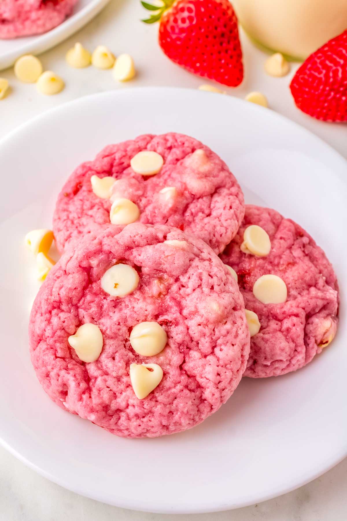 Three white chocolate chip strawberry cookies on a white plate.