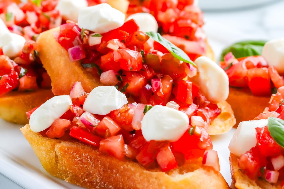 Pieces of Bruschetta with Mozzarella on a white serving platter.