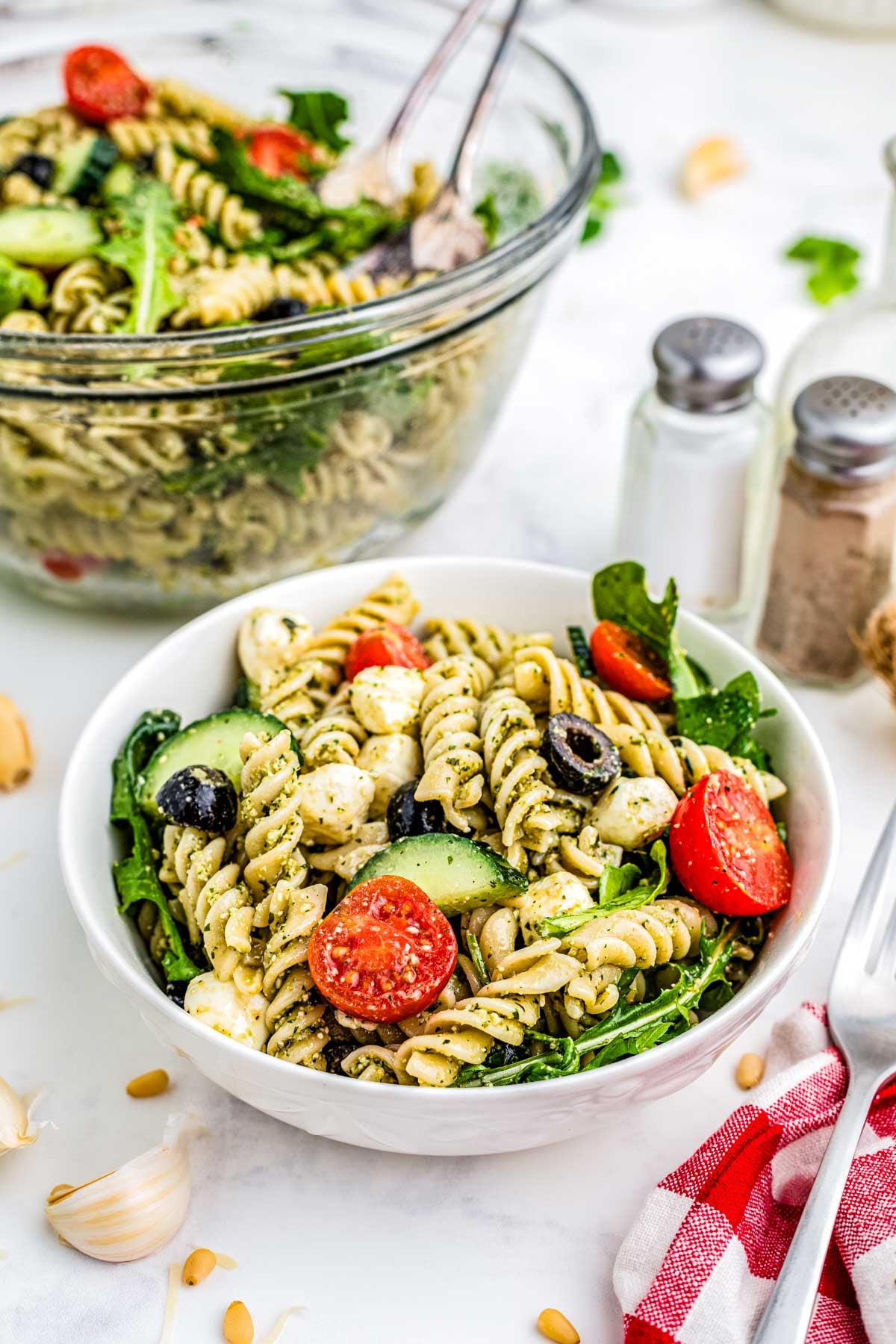 Pesto Pasta Salad in a white salad bowl with salt and papper and a napkin nearby.