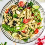 Summer Pesto Pasta Salad in a clear serving bowl with tongs.