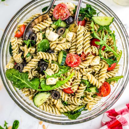 Summer Pesto Pasta Salad in a clear serving bowl with tongs.