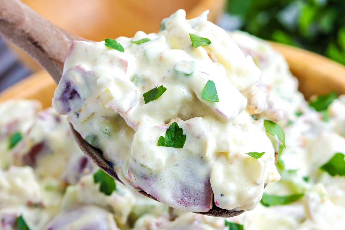 A scoop of no egg potato salad on a wooden serving spoon.