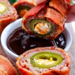 A Smoked Armadillo Egg cut in half and then a hand dipping it into BBQ sauce.