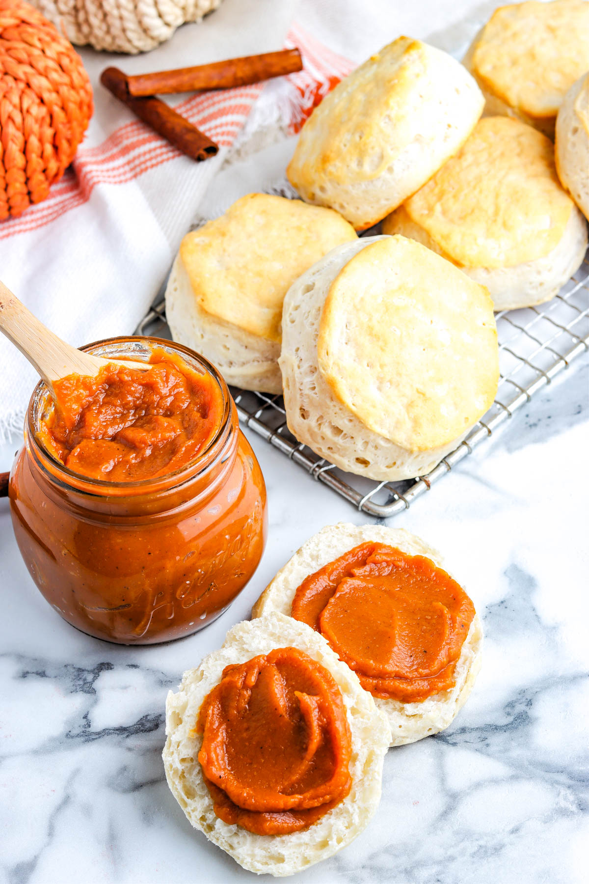 Jar of homemade spiced pumpkin butter with a wooden spoon, served on fluffy biscuits.
