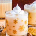 Rich and creamy eggnog in a gold snowflake glass with a swirl of whipped cream on top, perfect for the holidays.