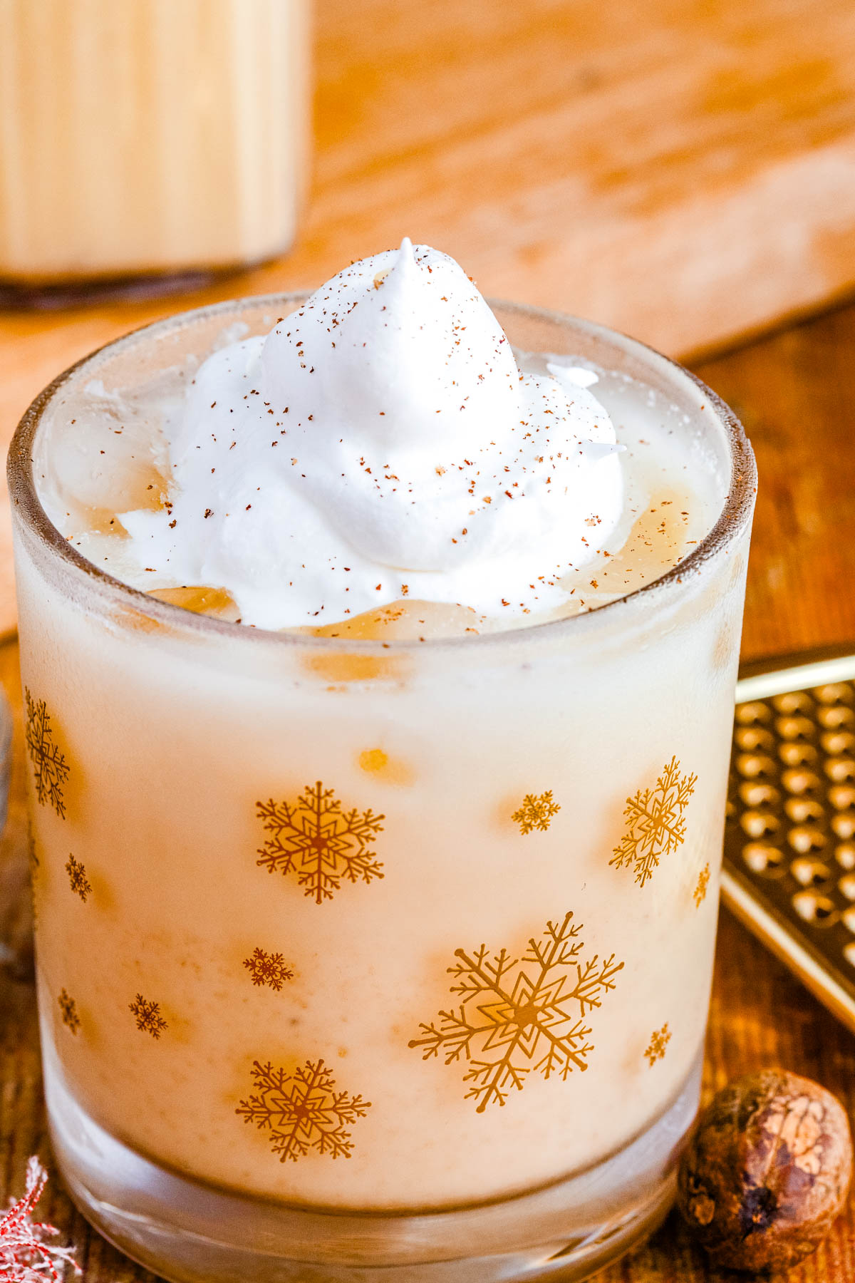 Close-up of creamy homemade eggnog in a snowflake glass topped with whipped cream and sprinkled with fresh nutmeg.
