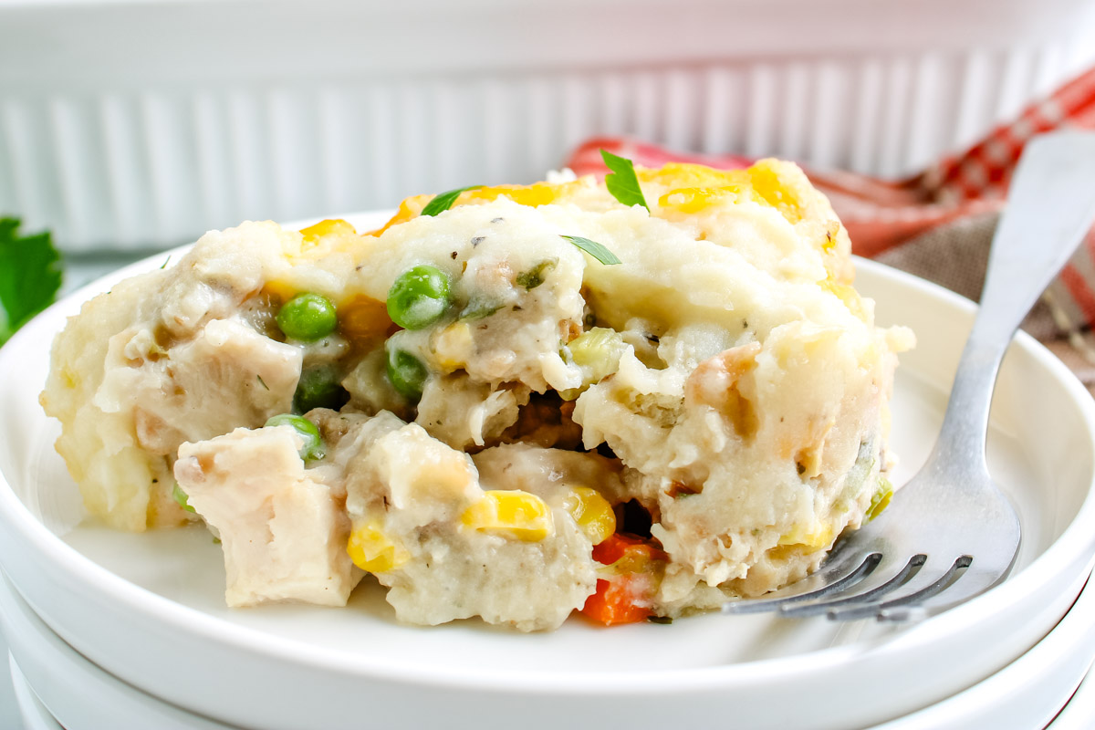 Serving of creamy leftover turkey casserole with peas, carrots, corn, and mashed potato topping on a white plate with a fork.
