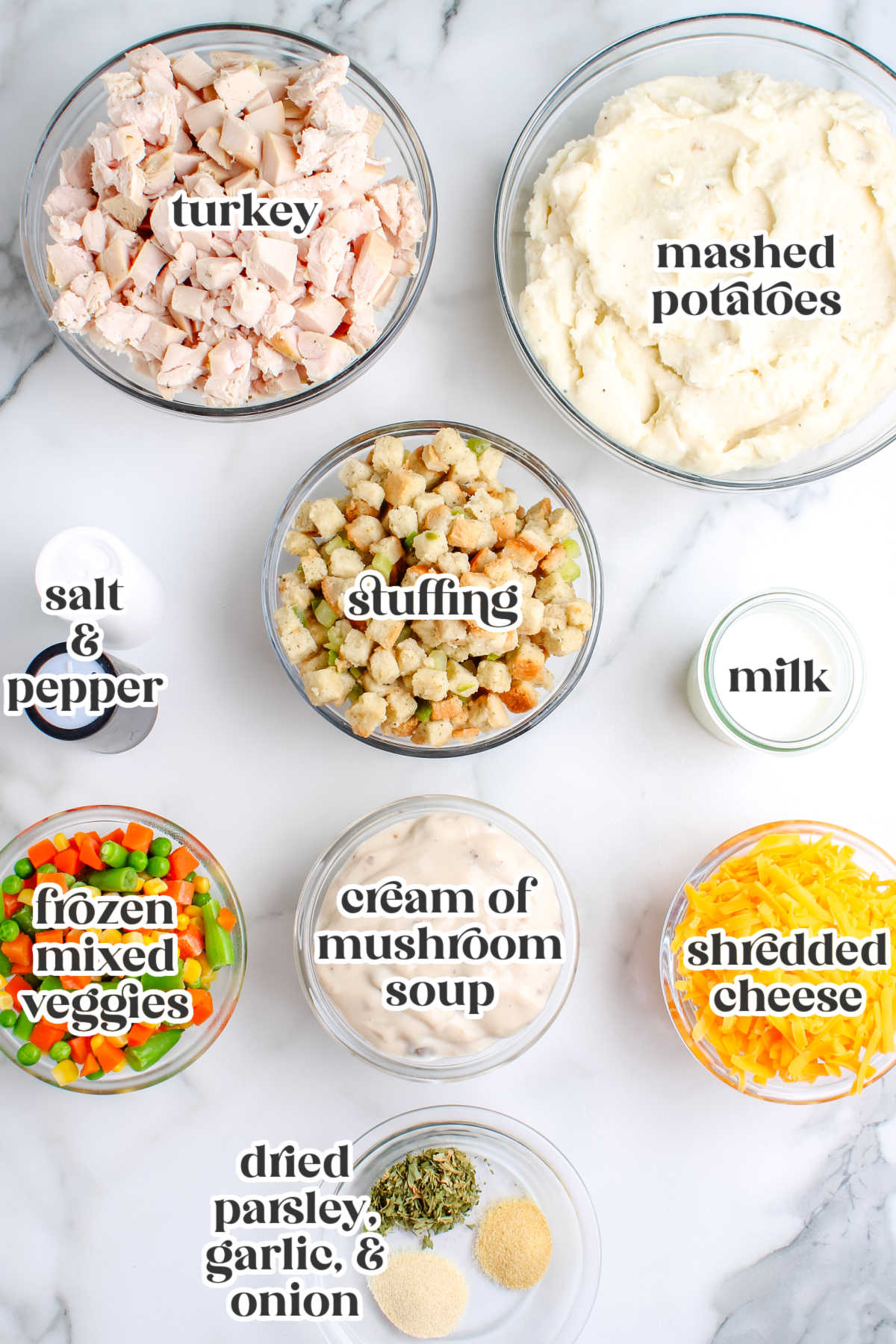Overhead view of leftover turkey casserole ingredients including cubed turkey, mashed potatoes, stuffing, frozen mixed vegetables, cream of mushroom soup, cheddar cheese, milk, and seasonings.